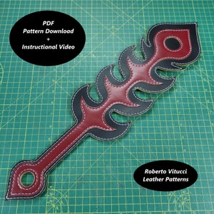 May include: A red and black leather paddle with a flame design. The paddle has a hole in the handle and is stitched with white thread. The text "PDF Pattern Download + Instructional Video" is in a white circle at the top of the image. The text "Roberto Vitucci Leather Patterns" is at the bottom of the image.