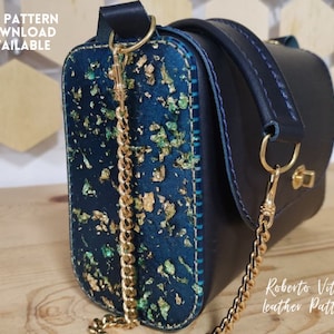 Puede incluir: Un bolso de mano de cuero azul oscuro con una correa de cadena dorada y detalles dorados. El bolso tiene un patrón verde y dorado en la parte delantera. El texto "Roberto Vitucci leather patterns" es visible en la esquina inferior derecha de la imagen.