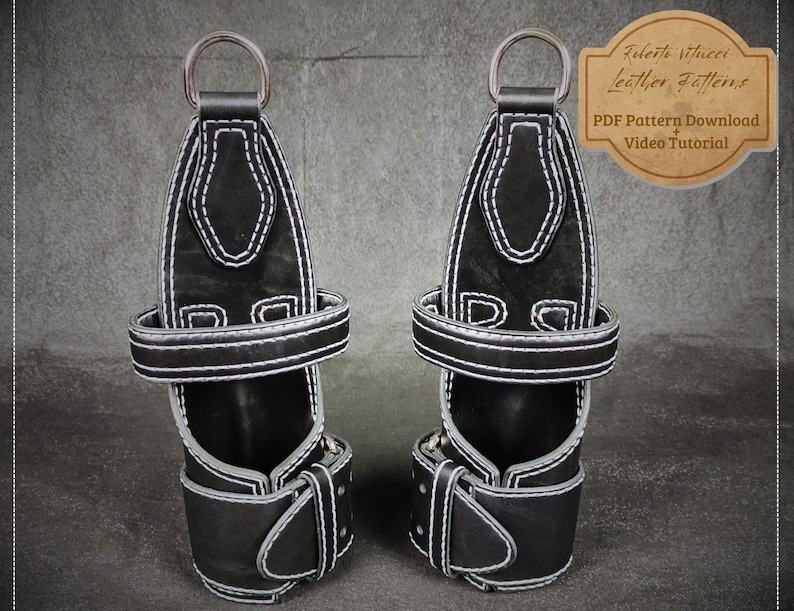 Op de afbeelding: Een paar zwarte leren polsbandjes met witte stiksels en zilveren metalen ringen. De bandjes zijn ontworpen voor gewichtheffen en hebben een gespsluiting. De tekst "Roberto Vitucci Leather Patterns" is zichtbaar in de rechterbovenhoek van de afbeelding. De tekst "PDF Pattern Download + Video Tutorial" is ook zichtbaar.