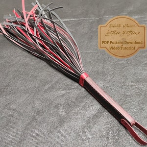 May include: A black and red leather whip with a braided handle. The whip is made of multiple strands of leather that are tied together at the end. The handle is wrapped in black leather and has a red leather loop at the end. The whip is on a gray textured surface. Roberto Vitucci Leather Patterns PDF Pattern Download + Video Tutorial