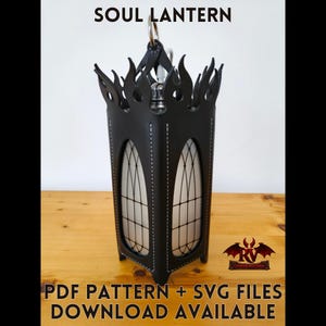 May include: Black leather lantern with flame-shaped cutouts at the top and arched window designs. The lantern has a silver metal handle and is lit from within. The text "SOUL LANTERN" is at the top. The text "PDF PATTERN + SVG FILES DOWNLOAD AVAILABLE" is at the bottom.