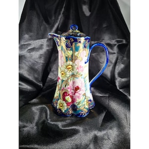 May include: A porcelain coffee pot featuring a scalloped base and rim, decorated with vibrant pink and yellow floral patterns, intricate gold filigree accents, and a deep cobalt blue handle, spout, and lid with a small knob finial.