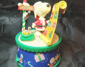 Snoopy como Papá Noel revisando su lista. Caja de música. Suena "Te deseamos una Feliz Navidad".