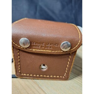 May include: A brown leather case with a textured surface, featuring yellow contrast stitching and two silver-colored metal snap buttons on the front flap. The text GENUINE LEATHER MADE IN U.S.A. is embossed on the front flap above the snap buttons.