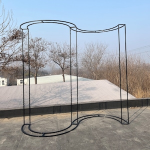 May include: Black metal archway with a curved design. The archway is standing on a concrete surface.