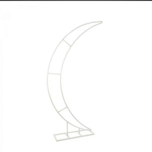 May include: White metal crescent moon arch stand for wedding or event decor. The stand is made of metal tubing and has a simple, modern design.