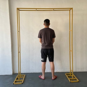 Könnte beinhalten: Ein goldfarbener Metallbogen mit schlichtem Design. Der Bogen steht auf einem Betonboden.