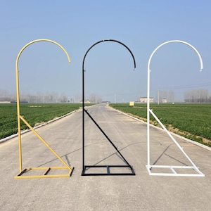 May include: Three metal stands with a curved top bar. The stands are gold, black, and white. The stands are on a paved road with green grass on either side.