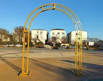 May include: A gold metal archway with a rounded top and a rectangular base. The archway is standing on a paved surface.