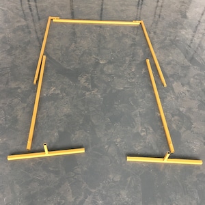 May include: A gold metal archway kit, disassembled, with four pieces. The archway is made of thin metal tubing and is designed to be assembled into a rectangular shape.