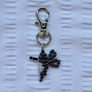 May include: A silver-colored metal keychain with a lobster clasp and a beaded dragonfly charm. The dragonfly is made of black, iridescent, and white beads, and has a small black body.