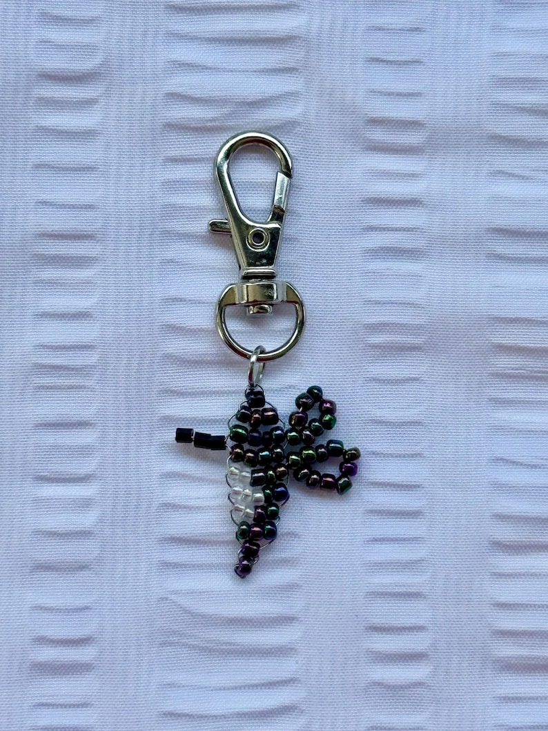 May include: A silver-colored metal keychain with a lobster clasp and a beaded dragonfly charm. The dragonfly is made of black, iridescent, and white beads, and has a small black body.