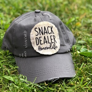 Könnte beinhalten: Graue, abgenutzte Baseballkappe mit einem weißen Patch, auf dem "Snack Dealer #momlife" steht.