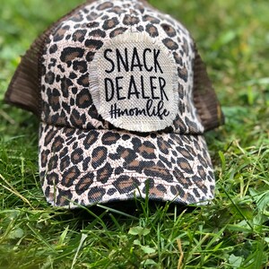 Könnte beinhalten: Eine braune und schwarze Trucker-Kappe mit Leopardenmuster und einem weißen Patch mit der Aufschrift "Snack Dealer #momlife".