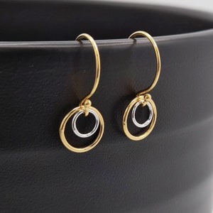 May include: A pair of gold hoop earrings with a smaller silver hoop inside each. The earrings are hanging from a black surface.