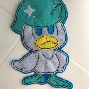 May include: A felt appliqué of a duck wearing a teal blue helmet with a white star. The duck has a yellow beak and blue eyes. The duck's feet are teal blue.