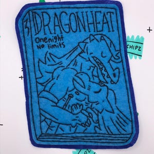May include: A blue felt patch with the text "DRAGONHEAT" and the words "One night No limits". The patch features a black line drawing of a dragon and a person. The patch has a dark blue border.
