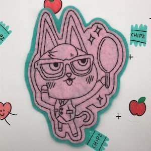 May include: A pink felt patch with an outline of a cartoon cat wearing glasses and holding a magnifying glass. The cat has a pink nose and a black outline. The patch is surrounded by a teal felt border. The words "CHIPZ" are written on two teal felt tags.