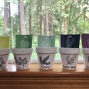 May include: Five white terracotta pots with black hand-painted illustrations of herbs. The pots are labeled "Cilantro", "Dill", "Thyme", "Sweet Basil", and "Oregano".