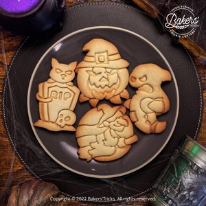 May include: Four Halloween-themed cookie cutters on a black plate. The cutters are shaped like a pumpkin, a ghost, a witch, and a cat with a tombstone. The cutters are made of metal and have a shiny finish.