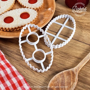 Peut inclure: Deux emportes-pièces en plastique blanc en forme d'ovale avec un bord festonné. Les emportes-pièces ont un motif de grille à l'intérieur. Les emportes-pièces sont sur une surface en bois.