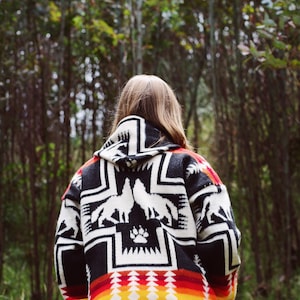 May include: A person wearing a black and white hooded jacket with a red, orange, and yellow geometric pattern on the bottom. The jacket features a design of two wolves howling at the moon.
