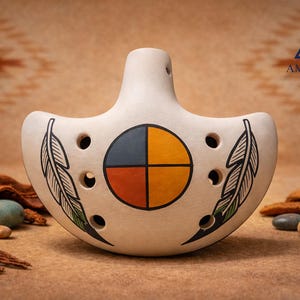 May include: Cream-colored ceramic ocarina with a central circular design divided into four colored quadrants: blue, yellow, orange, and black. Black feather designs flank the sides. The logo "Amerinkas Native Art" is visible.