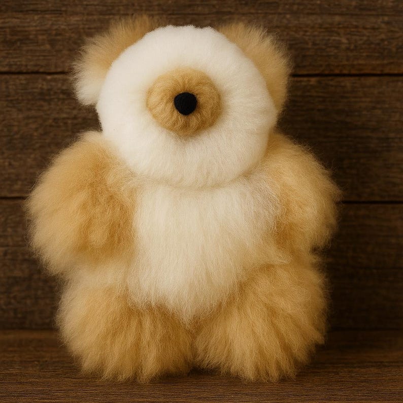 May include: A plush teddy bear made of soft, fluffy alpaca wool. The bear has a cream-colored face and body, with tan-colored arms, legs, and ears. It has a black button eye and a tan nose. The bear is a cuddly toy.