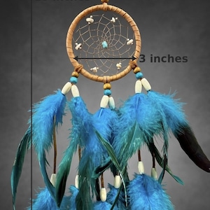 May include: A handcrafted dreamcatcher, 15 inches long and 3 inches wide, featuring a woven web within a tan hoop. It has blue feathers, wooden beads, and a central turquoise stone. The dreamcatcher is designed for wall hanging.