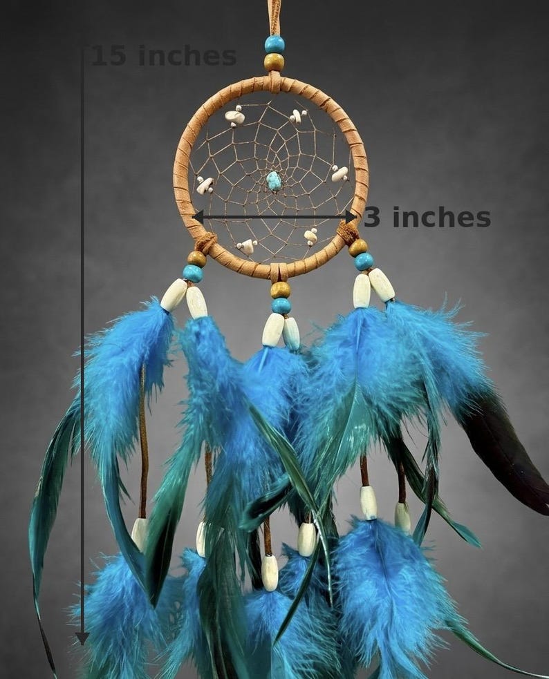 May include: A handcrafted dreamcatcher, 15 inches long and 3 inches wide, featuring a woven web within a tan hoop. It has blue feathers, wooden beads, and a central turquoise stone. The dreamcatcher is designed for wall hanging.