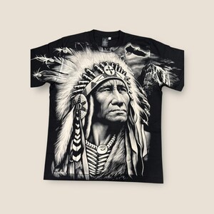May include: Black t-shirt with a white graphic print of a Native American chief wearing a headdress. The chief is looking to the right and has a serious expression on his face. The background of the graphic is a dark mountain scene with an eagle flying overhead.