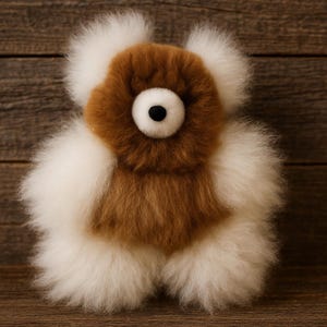 May include: A handmade plush toy in the shape of a bear, featuring a brown face and body with white accents. The bear has a large, central eye with a black pupil. The toy is made of soft, fluffy material.