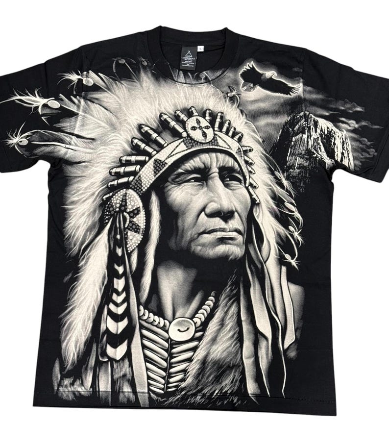May include: Black t-shirt with a white graphic print of a Native American chief wearing a headdress. The chief is looking to the right and has a serious expression on his face. The background of the image is a mountain range with a bald eagle flying overhead.