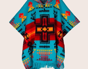 Puede incluir: Un poncho turquesa con capucha y flecos, con un patrón geométrico en rojo, naranja, amarillo y negro. El diseño incluye un motivo central en forma de cruz y varias formas de flecha. El poncho está hecho de material tejido.