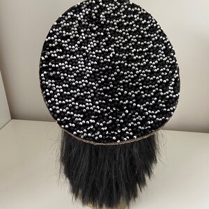 K&ouml;nnte beinhalten: Eine schwarze Baskenm&uuml;tze mit einem runden Design aus schwarzen und silbernen Pailletten.