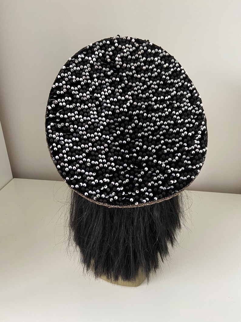 K&ouml;nnte beinhalten: Eine schwarze Baskenm&uuml;tze mit einem runden Design aus schwarzen und silbernen Pailletten.