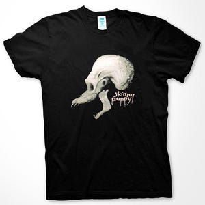 Puede incluir: Camiseta negra con un gráfico blanco de una calavera con la boca abierta y el texto "skinny puppy" en rosa.