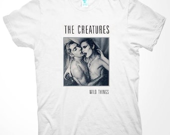 Könnte beinhalten: Weißes T-Shirt mit einem Schwarz-Weiß-Bild von zwei sich umarmenden Personen. Der Text "THE CREATURES" steht über dem Bild und "WILD THINGS" darunter. Das Shirt hat einen Rundhalsausschnitt und kurze Ärmel.