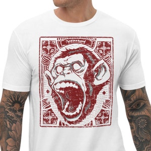 Puede incluir: Camiseta blanca con un gráfico rojo y blanco de un mono gritando en un marco desgastado.