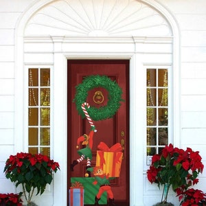 May include: A red front door with a green wreath and a candy cane hanging from it. Two elves are climbing the candy cane, one holding a large gift box with a red bow. The door is surrounded by red poinsettia plants.