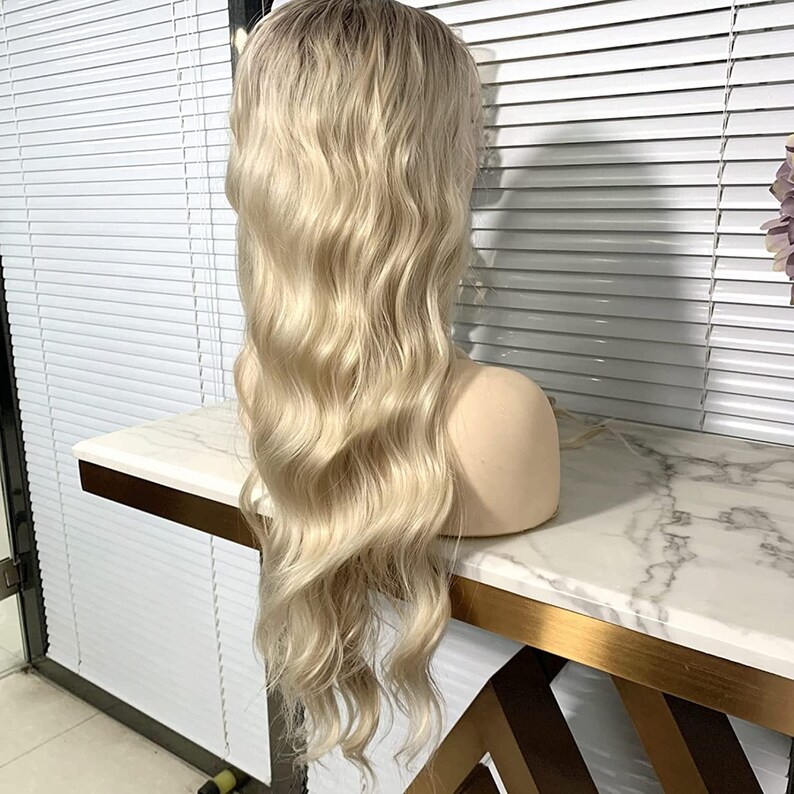 May include: A long, wavy blonde wig with a light brown root. The wig is styled in loose waves and falls to the shoulders.