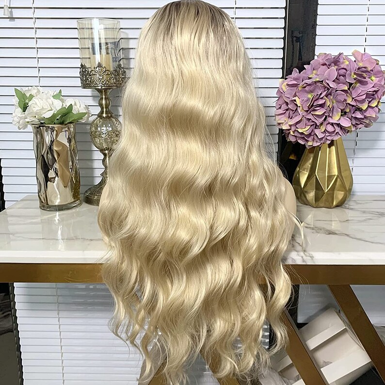 May include: A long, wavy blonde wig with a light brown root. The wig is styled in loose waves and falls to the shoulders.