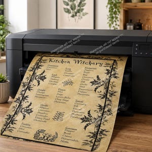 May include: A black printer printing a parchment-style paper with the words "Kitchen Witchery" and a list of herbs and their uses. The paper has a decorative border and is set on a wooden table.