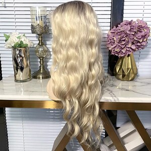May include: A long, wavy blonde wig with a light brown root. The wig is styled in loose waves and falls to the shoulders.