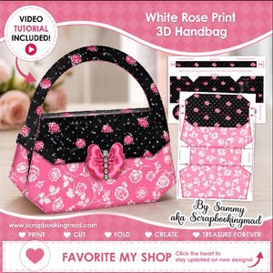 Könnte beinhalten: Eine rosa und schwarze 3D-Handtasche mit weißem Rosenmuster. Die Handtasche hat eine rosa Schleife mit einem Strassstein in der Mitte. Der Griff und die obere Klappe sind schwarz mit rosa Rosen. Der Text "White Rose Print 3D Handbag" ist enthalten.