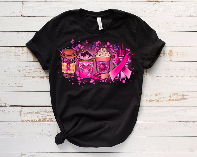 May include: Black t-shirt with a pink ribbon design featuring four coffee cups with pink and brown accents. The cups are decorated with butterflies and pink ribbons.