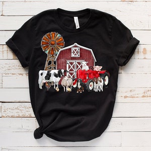 K&ouml;nnte beinhalten: Schwarzes T-Shirt mit einem roten Stall, einer Windm&uuml;hle, einem roten Traktor und Nutztieren. Zu den Tieren geh&ouml;ren eine Kuh, ein Schaf, ein Schwein und ein Hund.