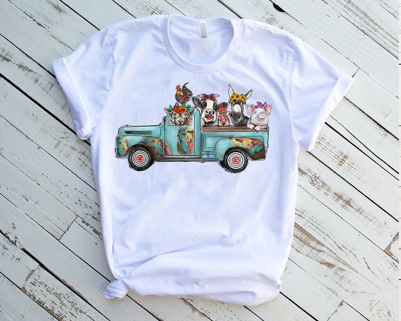May include: A white t-shirt featuring a graphic of a blue vintage pickup truck carrying a cow, pig, donkey, goat, and rooster. The animals are wearing flower crowns.