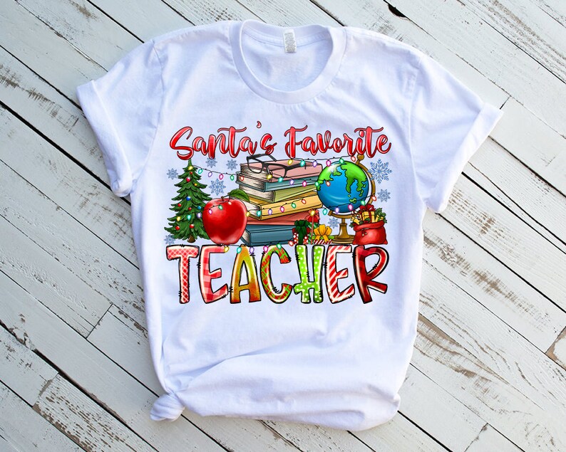 Puede incluir: Una camiseta blanca de manga corta con un estampado gr&aacute;fico que incluye el texto Santa's Favorite TEACHER. El dise&ntilde;o muestra una pila de libros, un globo terr&aacute;queo, una manzana roja, un &aacute;rbol de Navidad y luces decorativas.