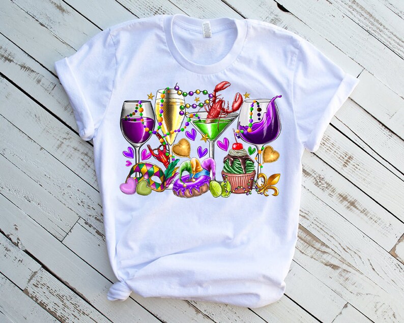 May include: White t-shirt with a colorful Mardi Gras design featuring glasses of wine, a martini, a cupcake, and beads.